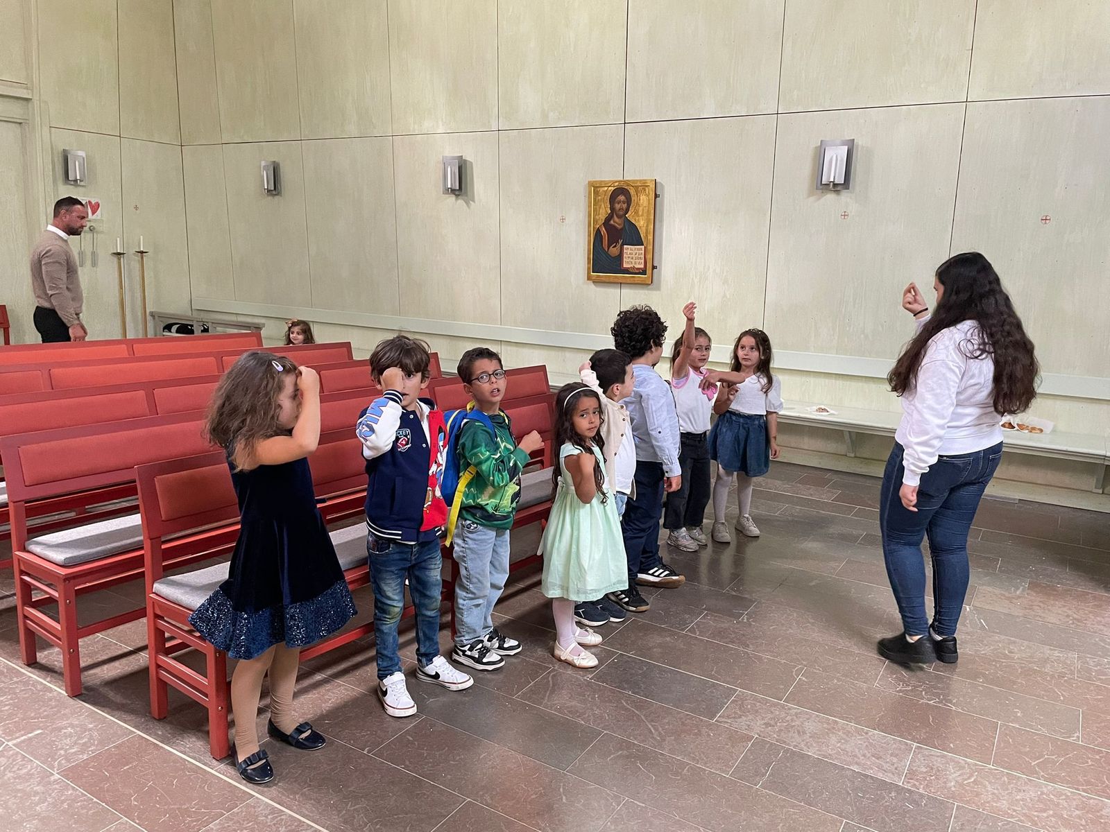 Barn står på rad i kyrkan och gör rörelser till en sång tillsammans med en ledare
