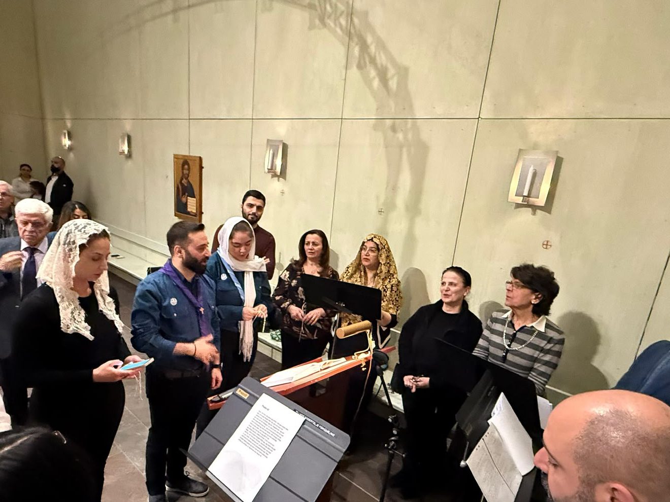 Kyrkokören sjunger vid notställen framme i kyrkan, flera av kvinnorna bär spetsslöjor