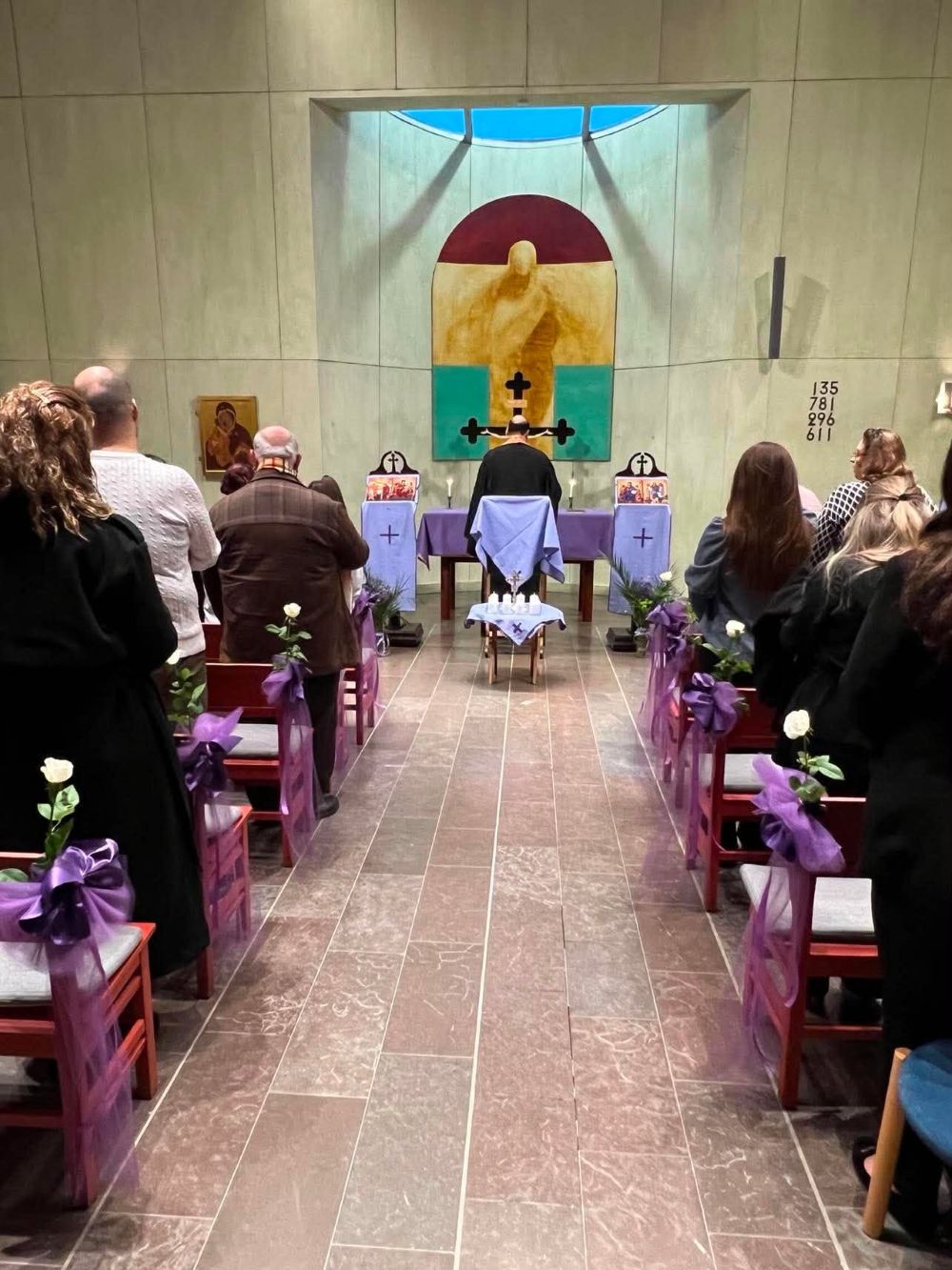 Kyrkorummet med blomstersmyckade bänkar och församlingen vid gudstjänsten