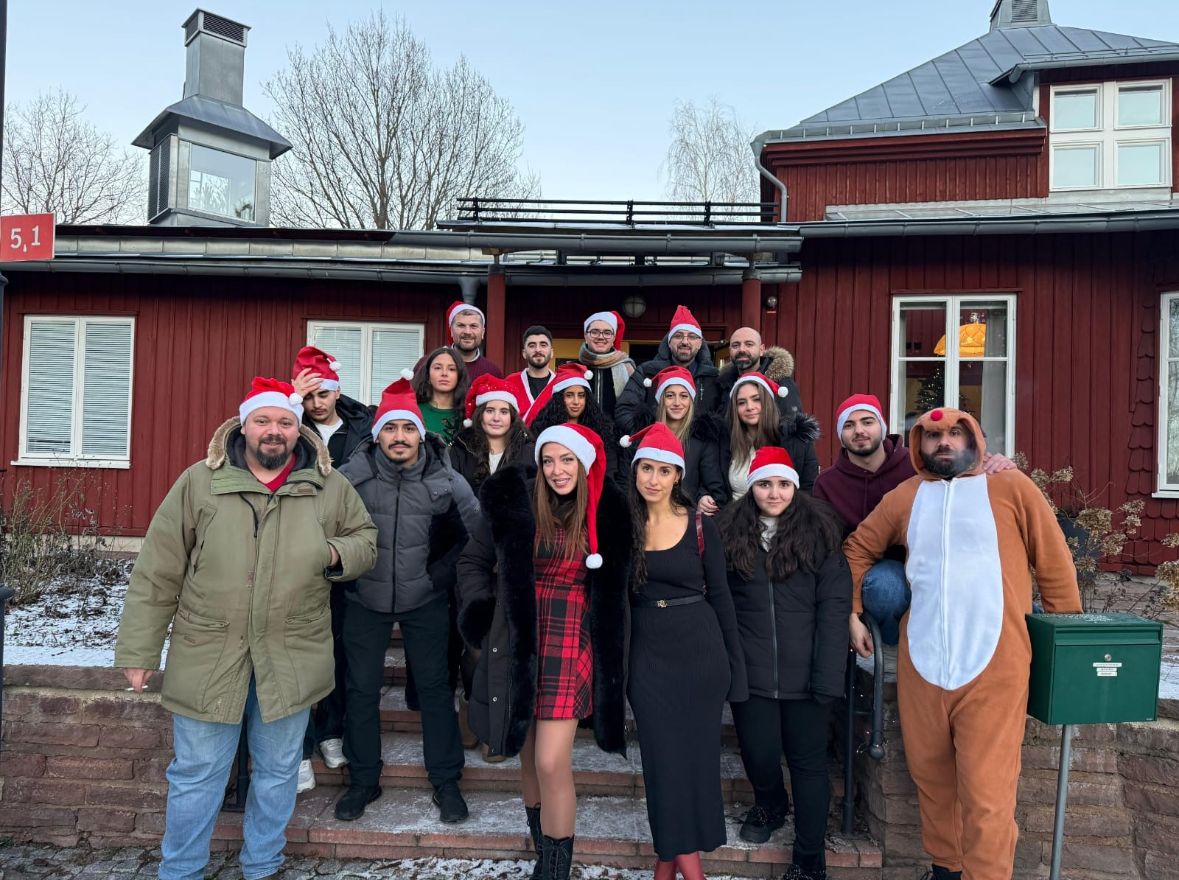 En grupp i tomteluvor samlad på trappan framför ett rött trähus i snön